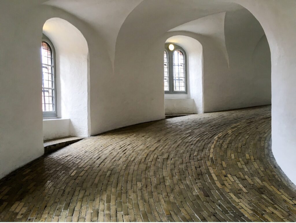 A spiral walkway with plaster walls and arched windows represents the WELL materials concept