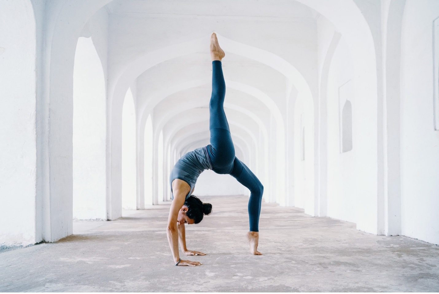 Woman doing a yoga backbend in a hallway of white arches represents the WELL movement concept