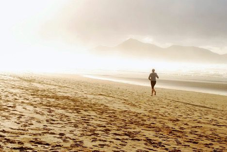 Woman running on the beach at sunrise represents the WELL movement concept