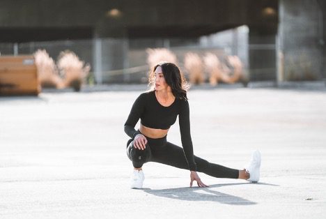Woman doing a low side lunge to stretch before a run represents the WELL movement concept