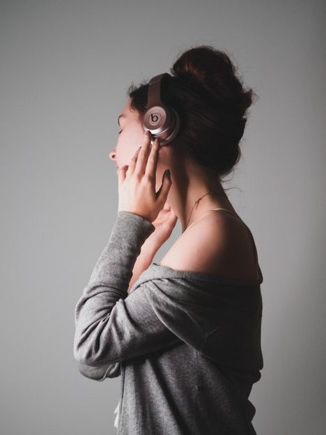 Woman listening to music on Beats headphones against a grey background represents the WELL sound concept