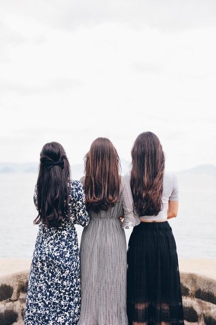 Three women standing with arms linked facing the ocean representing the WELL community concept